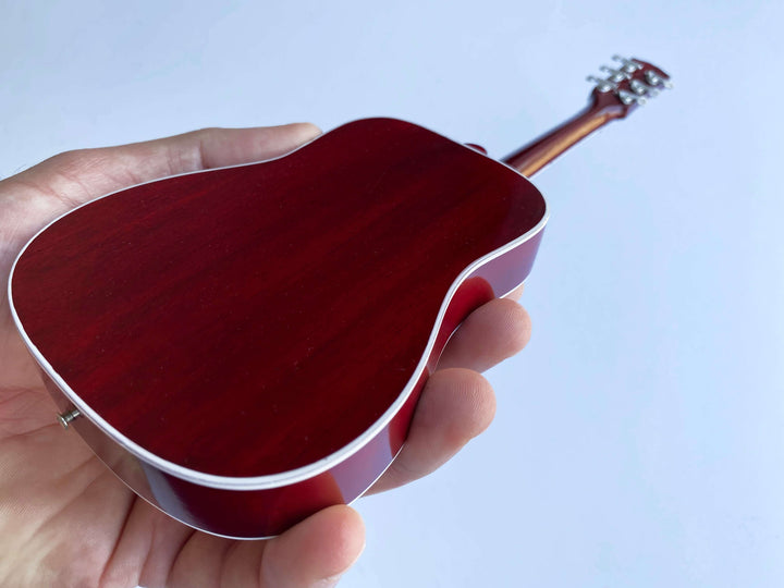 Hand holding Gibson Hummingbird Vintage Cherry Mini Guitar Replica showcasing vibrant cherry finish.