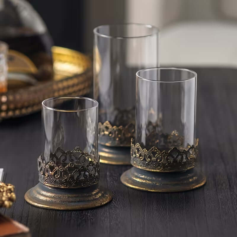 Three decorative glass candle holders with ornate bases on a dark surface