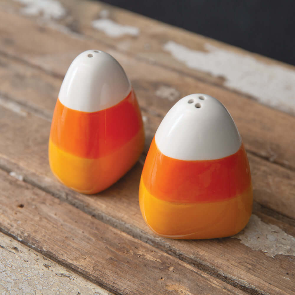 Candy Corn Ceramic Salt and Pepper Shaker Set with white, orange, and golden bands on a rustic wooden table; perfect for autumn decor.