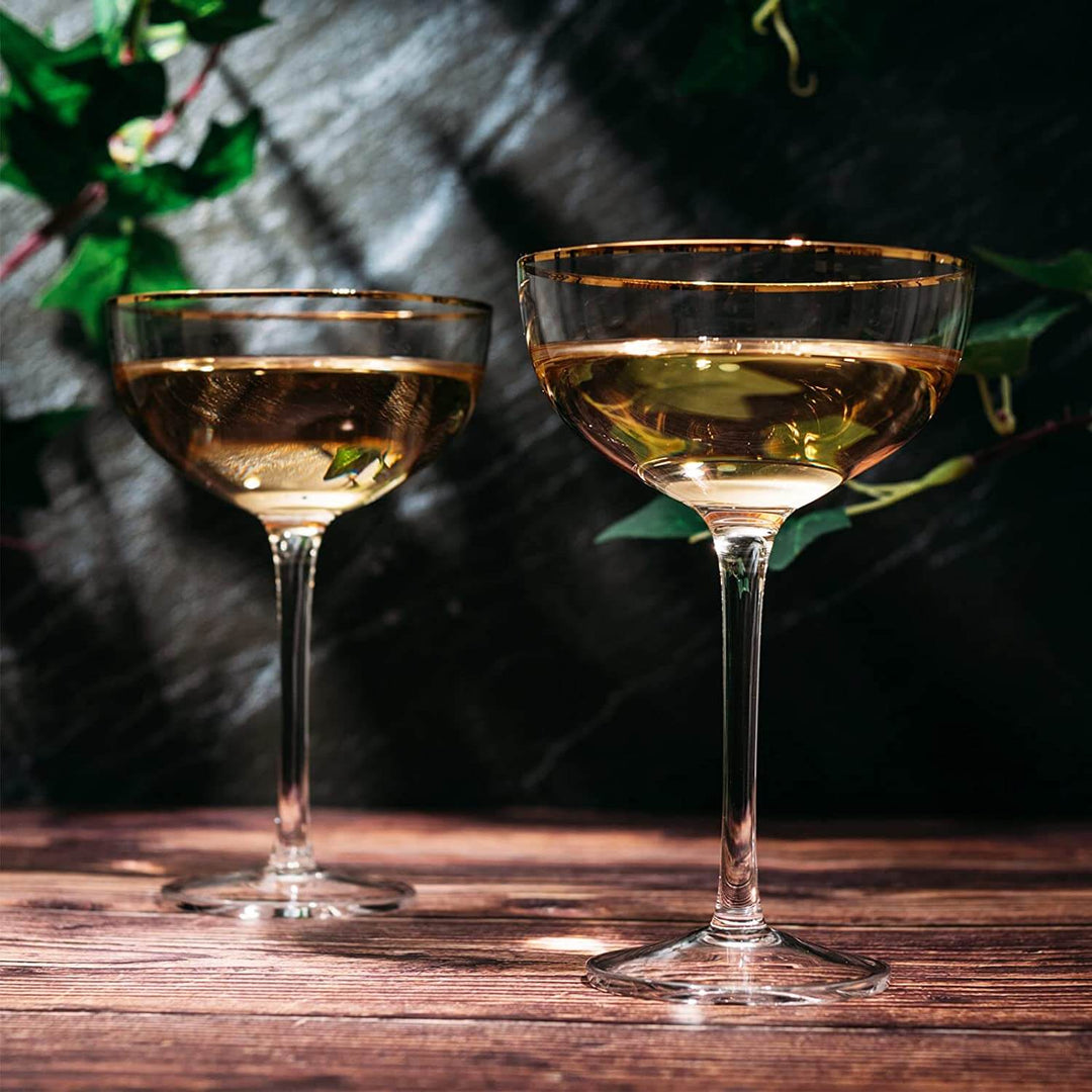 Two gold-rimmed cocktail glasses filled with a golden liquid on a wooden surface.