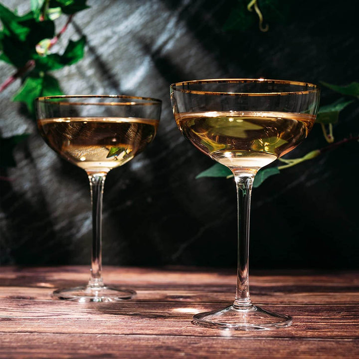 Two gold-rimmed cocktail glasses filled with a golden liquid on a wooden surface.