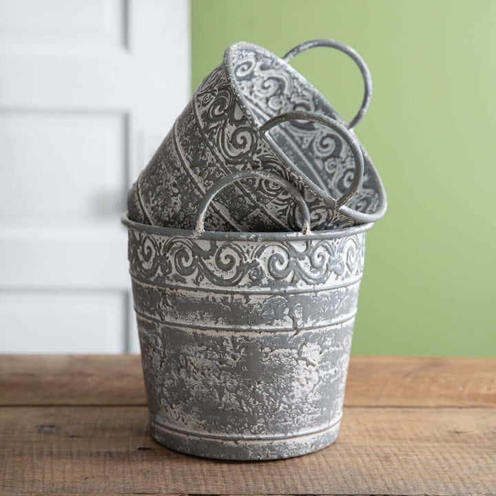 Set of 2 antique metal buckets with handles, featuring intricate filigree and distressed finish for vintage farmhouse decor.