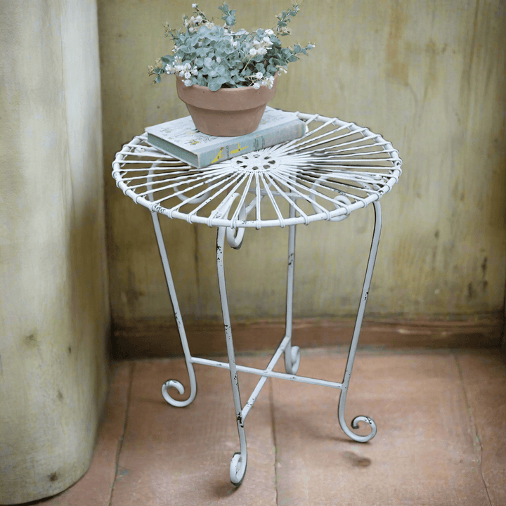 Rustic metal side table in white with a potted plant, showcasing a vintage wire design for indoor or outdoor decor.