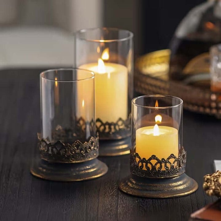 Three lit candles in decorative glass holders on a dark surface.
