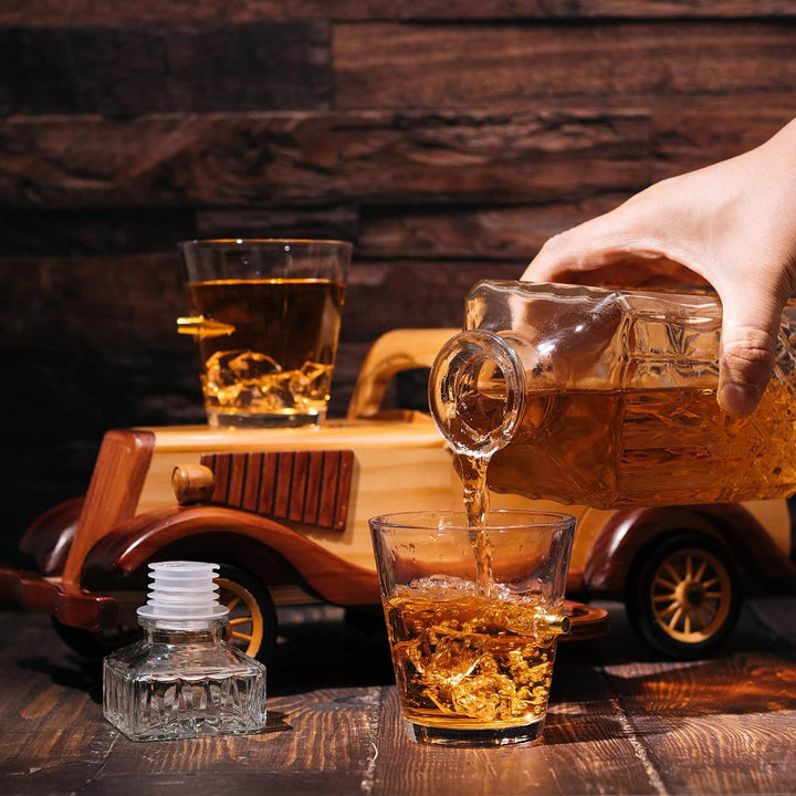 Person pouring whiskey from a decanter into a glass with a wooden car model in the background.