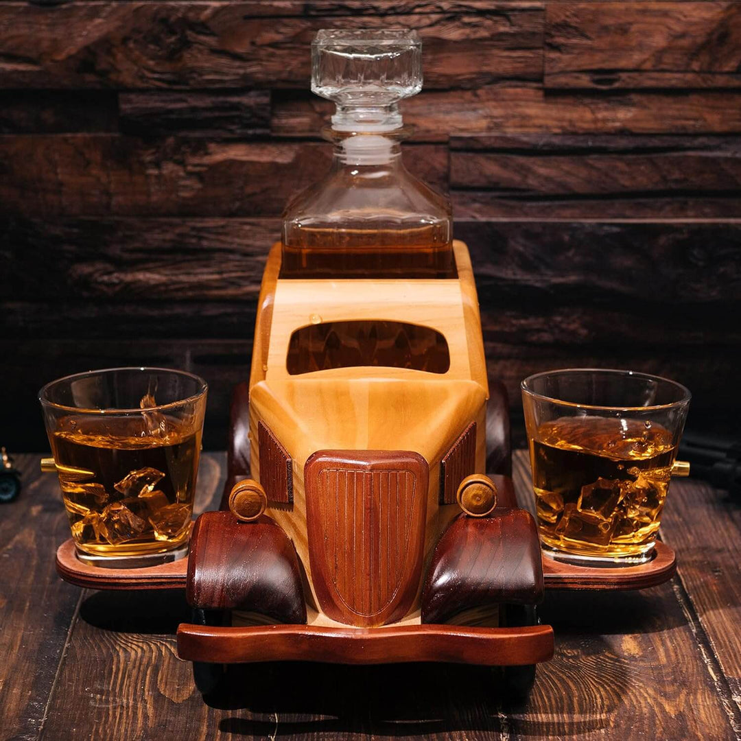 Wooden car-shaped decanter with two glasses of whiskey on a wooden surface.