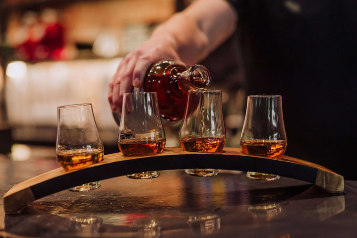 Person pouring whiskey into glasses on a wooden tray with a blurred background