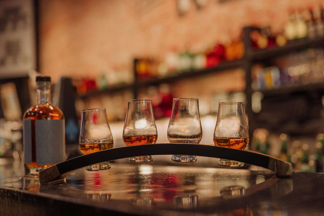 Four glasses of whiskey on a metal tray with a blurred bar background