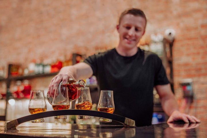Man pouring drinks into glasses at a bar with a warm ambiance.