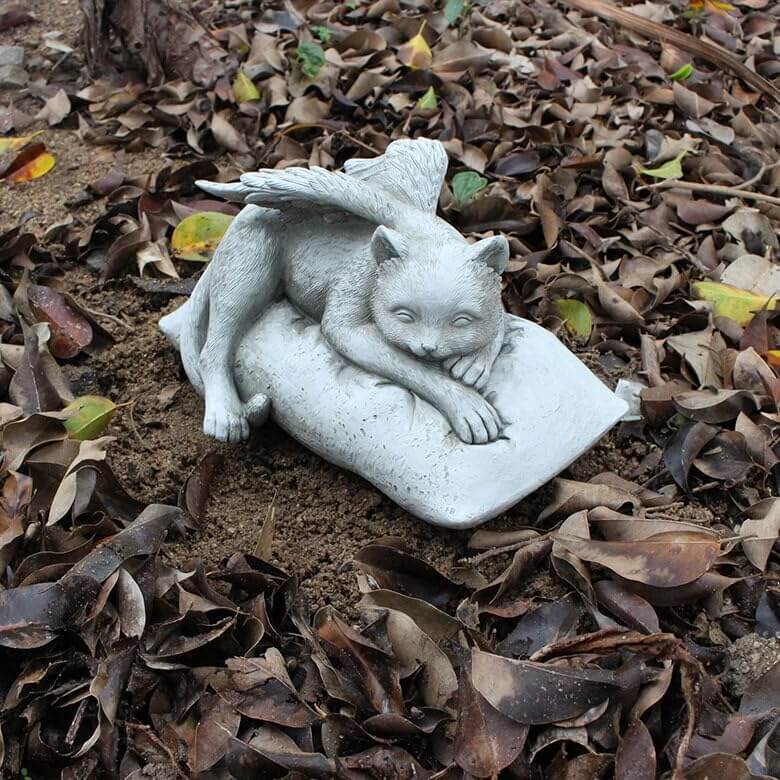 Angelic Cat Memorial Statue depicting a peaceful cat with angel wings resting on a cushion among fallen leaves.