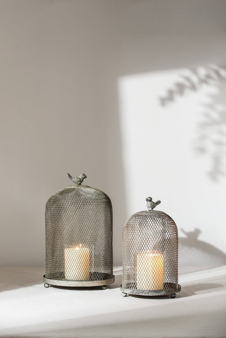 Two metal mesh candle holders with candles inside on a light surface.