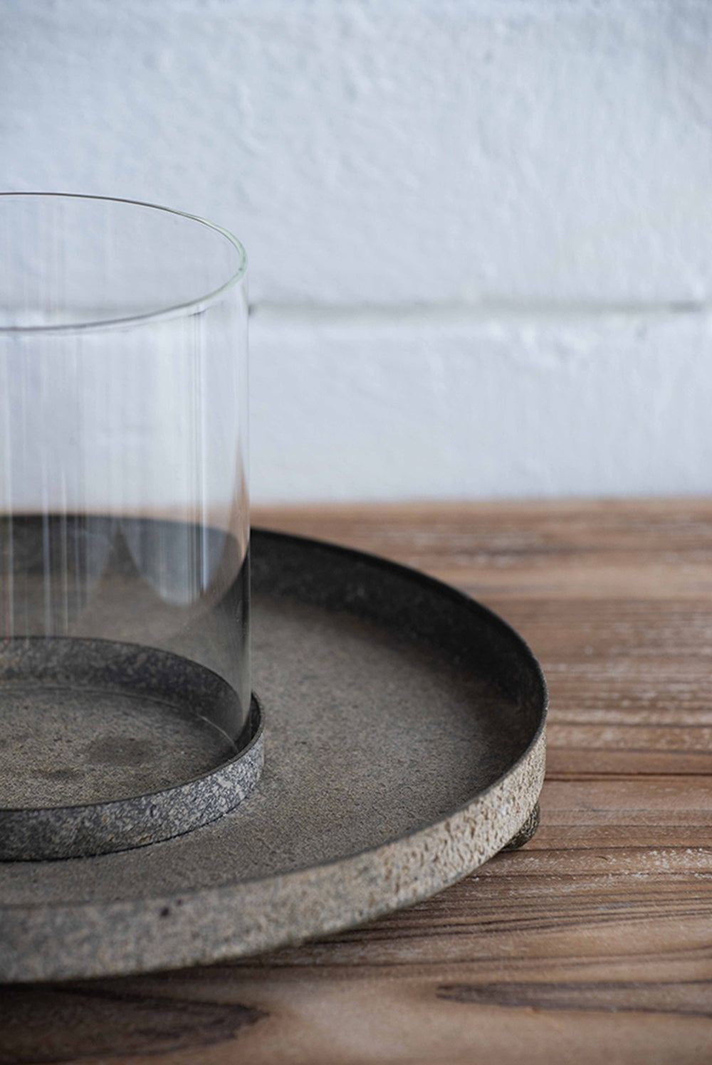 Clear glass candle holder on dark gray textured metal with a white wall background