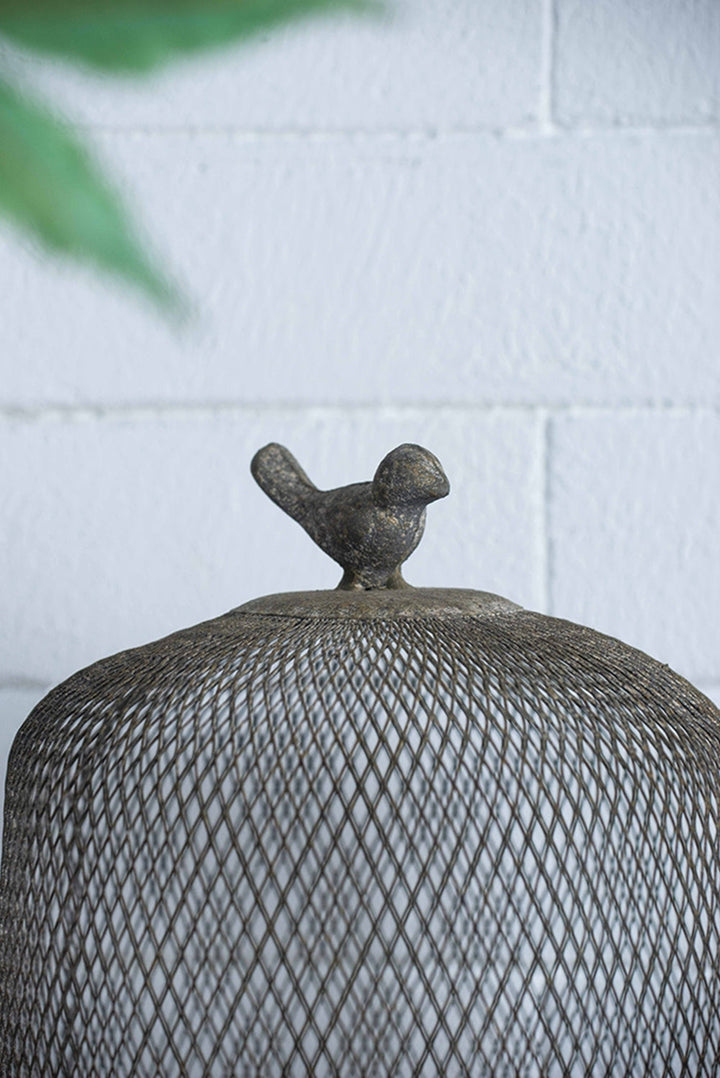 Decorative metal mesh dome with bird finial against a white brick wall