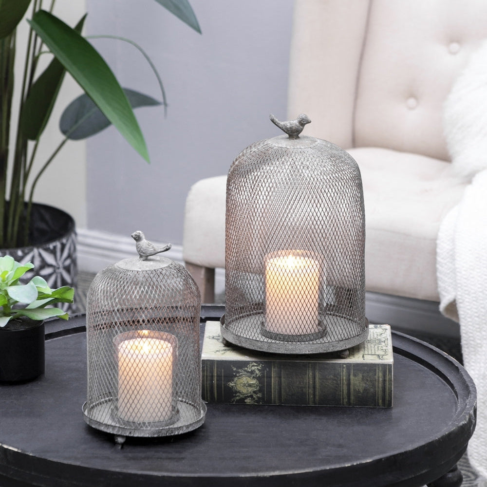 Decorative candles in mesh holders on a round wooden table with a white armchair in the background.