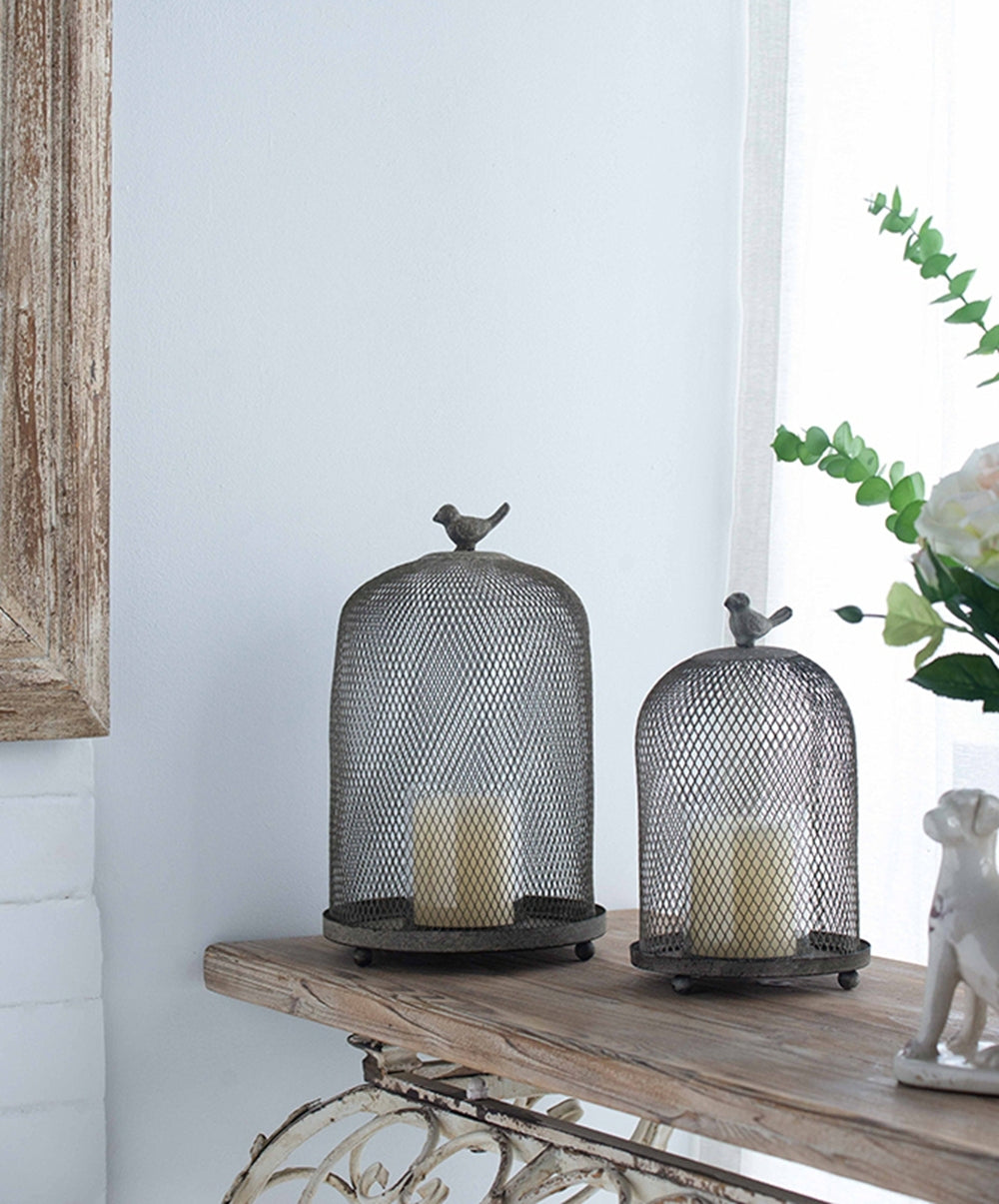 Decorative metal candle holders with birds on top on a wooden surface.
