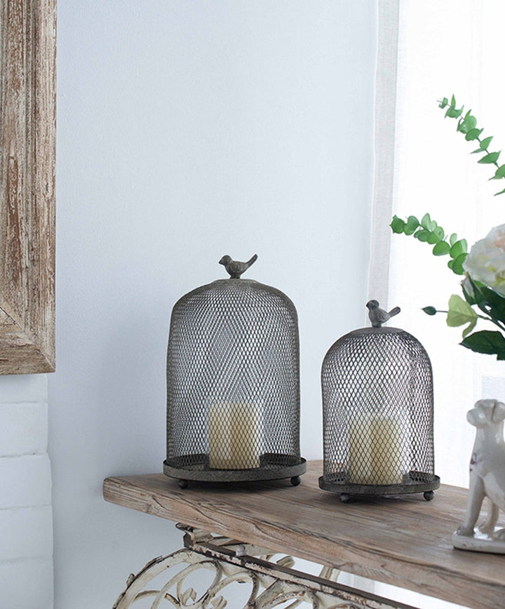 Decorative metal candle holders with birds on top on a wooden surface.