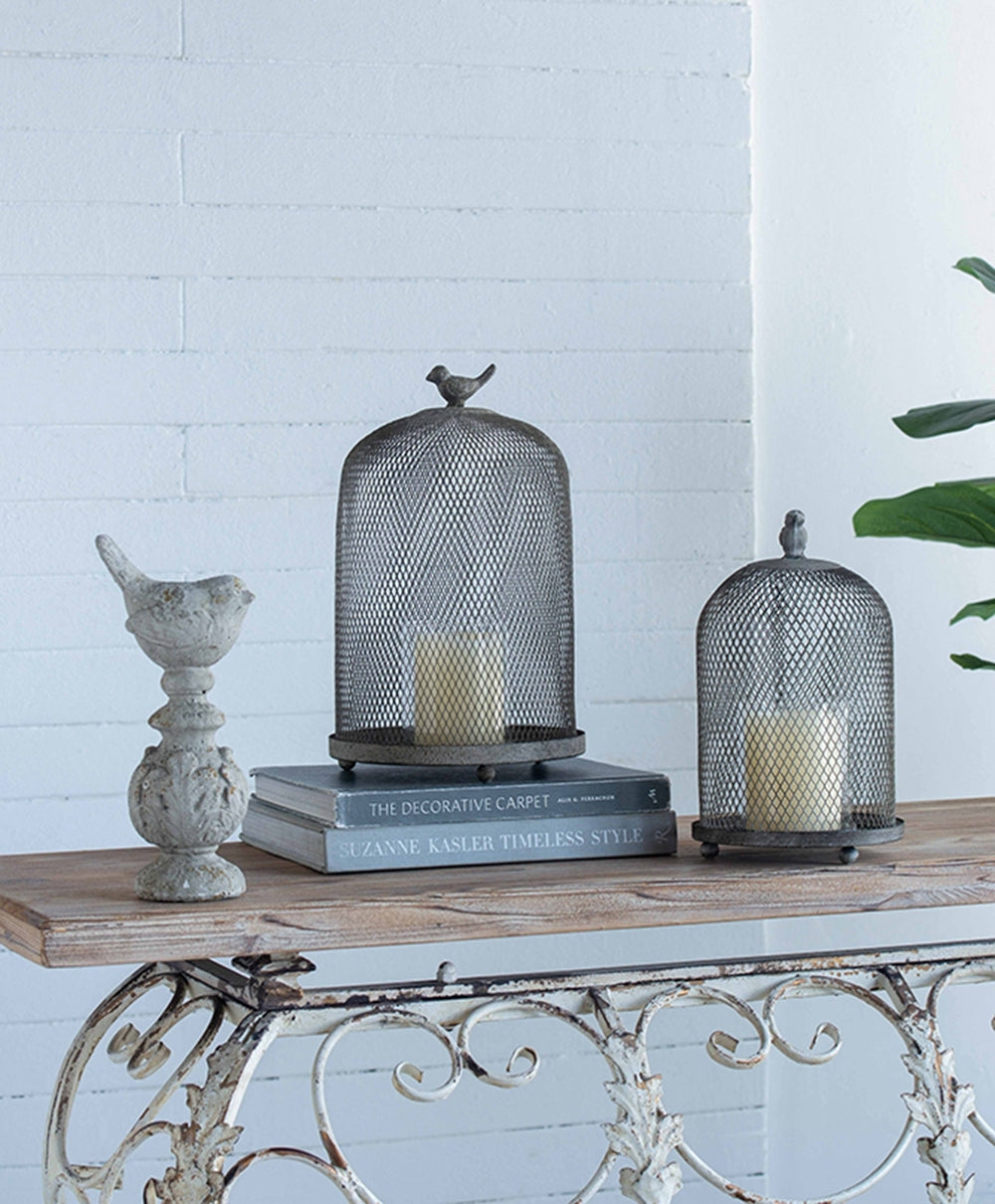 Decorative items including a birdcage, candle holder, and book on a wooden table with a white brick wall background.