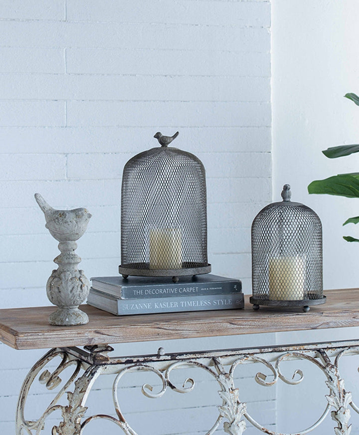Decorative items including a birdcage, candle holder, and book on a wooden table with a white brick wall background.