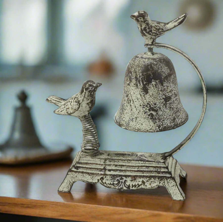 Whimsical antique cast iron bird counter bell with two sculpted birds and arched design on a wooden countertop.