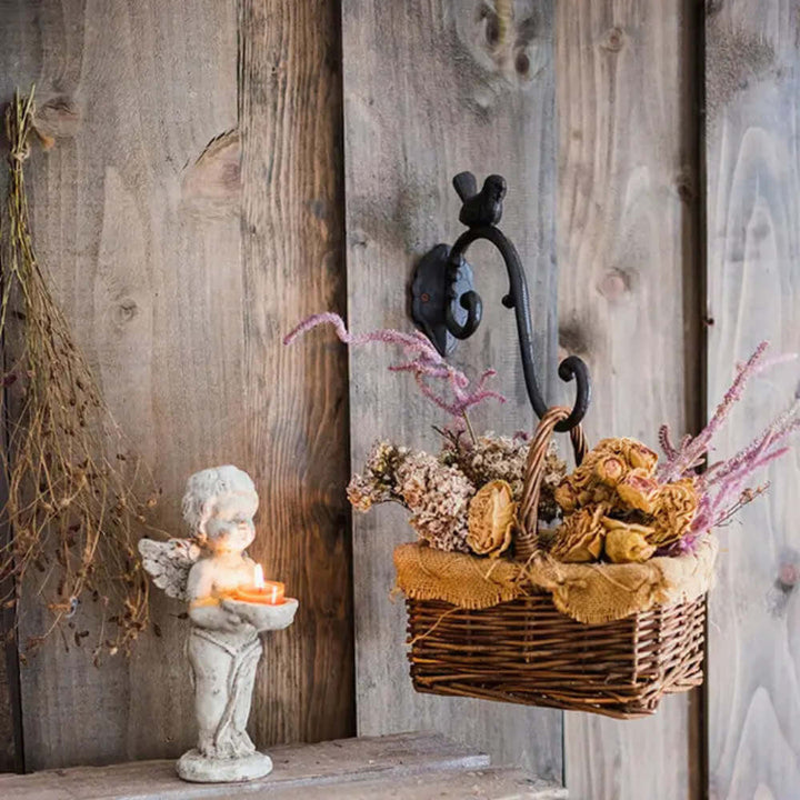 Antique cast iron bird wall hook displaying a basket of dried flowers beside a cherub candle holder in rustic decor.