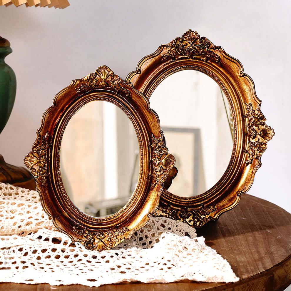 Two ornate gold mirrors on a textured surface with a blurred background