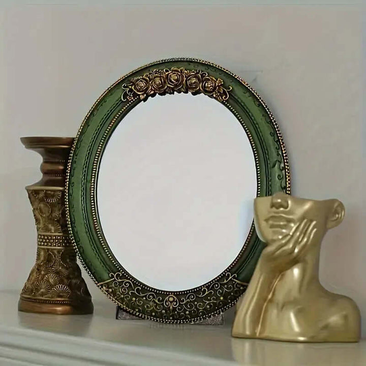 Antique green oval wall mirror with ornate gold detailing, paired with a decorative vase and bust sculpture.