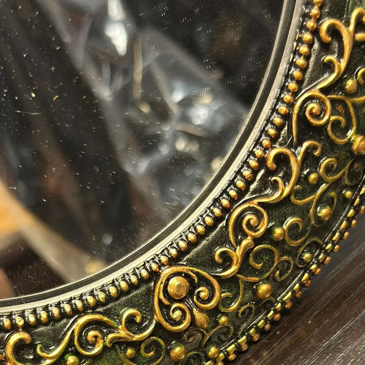 Close-up of ornate gold detailing on an antique green oval wall mirror showcasing intricate craftsmanship.