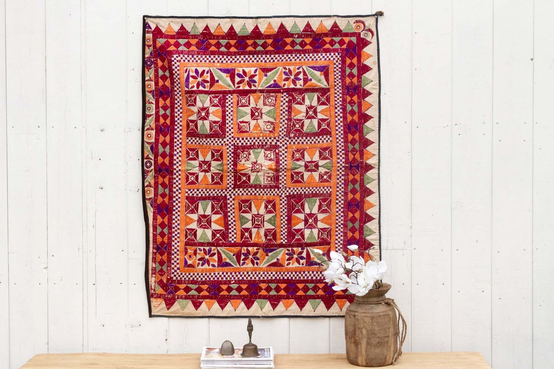 Colorful tapestry with geometric patterns hanging on a white wall above a wooden table.