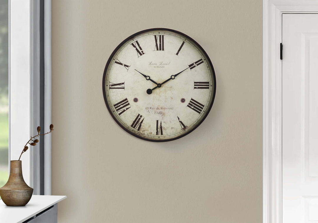 Decorative wall clock with Roman numerals on a beige wall.