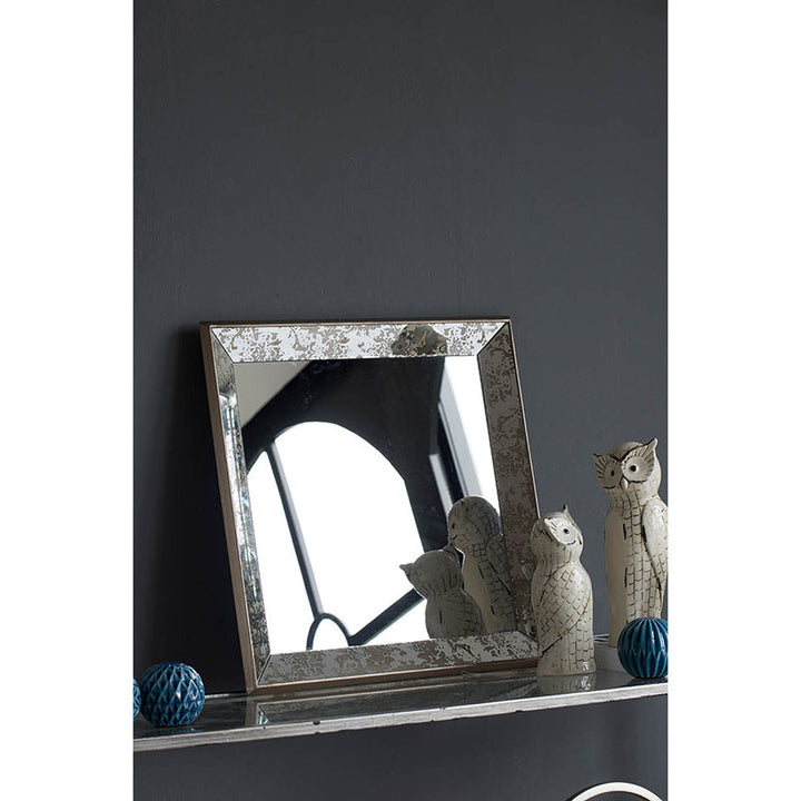 Decorative mirror with a textured frame on a dark surface with decorative items.