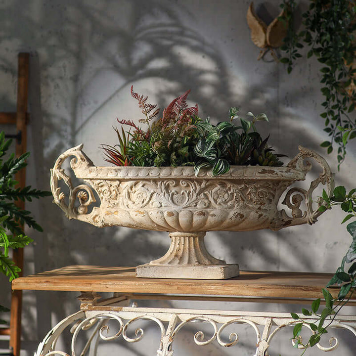Decorative urn with plants on a wooden table against a gray wall.