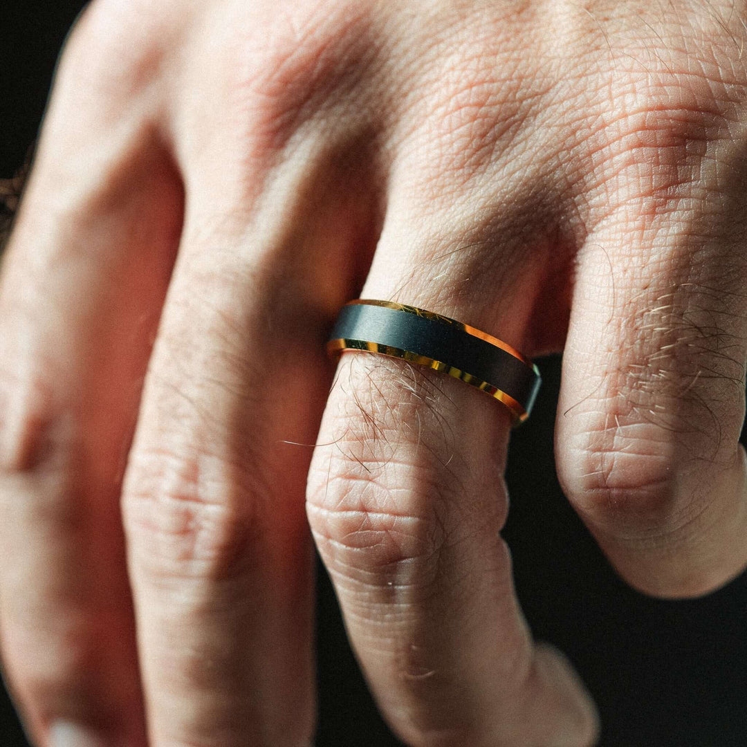 Close-up of a hand wearing a black and orange ring on a dark background