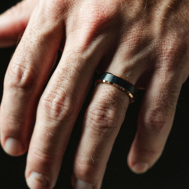 Close-up of a hand wearing a black and gold ring on a dark background