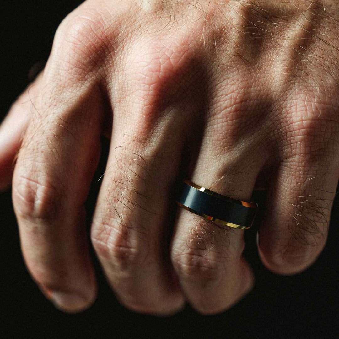 Close-up of a hand wearing a black and gold ring on a dark background