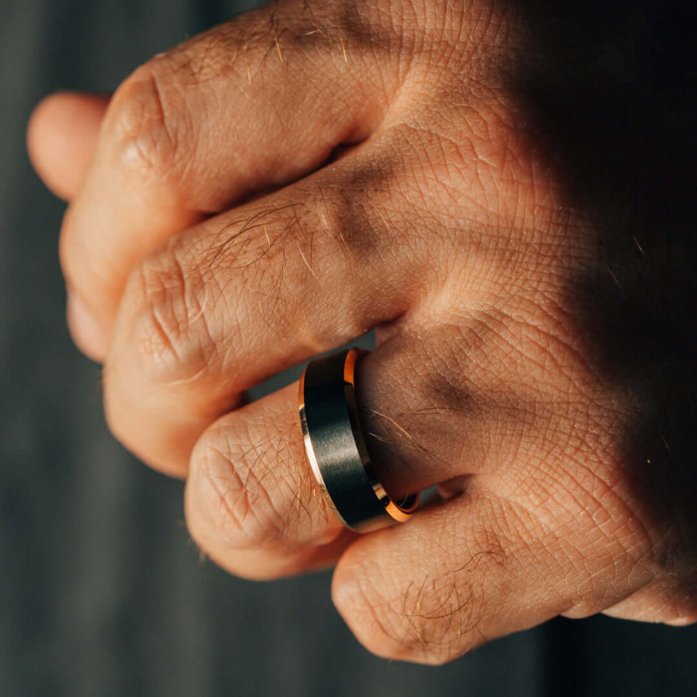 Close-up of a hand wearing a black ring with an orange accent on a dark background