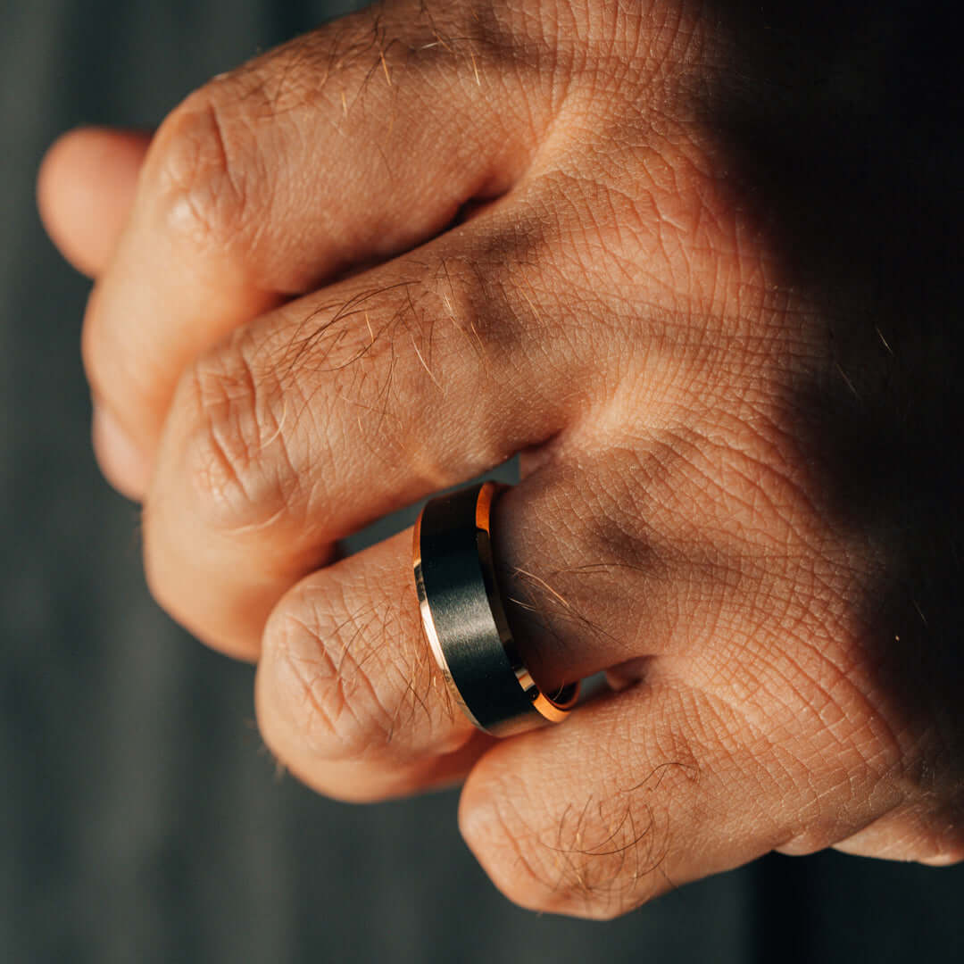 Close-up of a hand wearing a black ring with an orange accent on a dark background