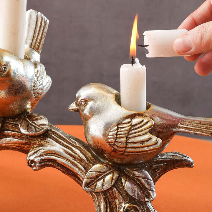 Decorative candle holder with bird design being lit by a hand.