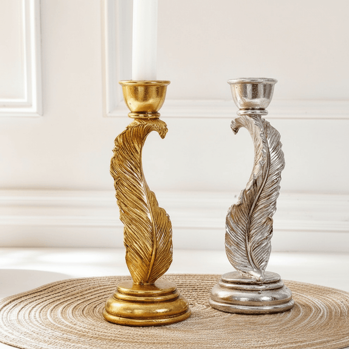 Gold and silver feather-shaped candle holders on a textured surface with a neutral background