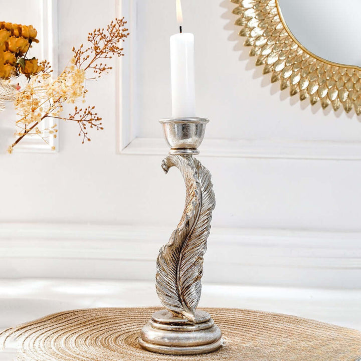 Decorative candle holder with a candle on a table, with flowers and a mirror in the background.