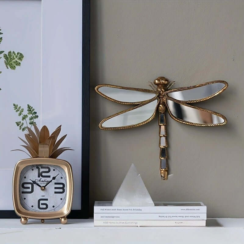 Decorative gold dragonfly wall art and clock on a shelf.
