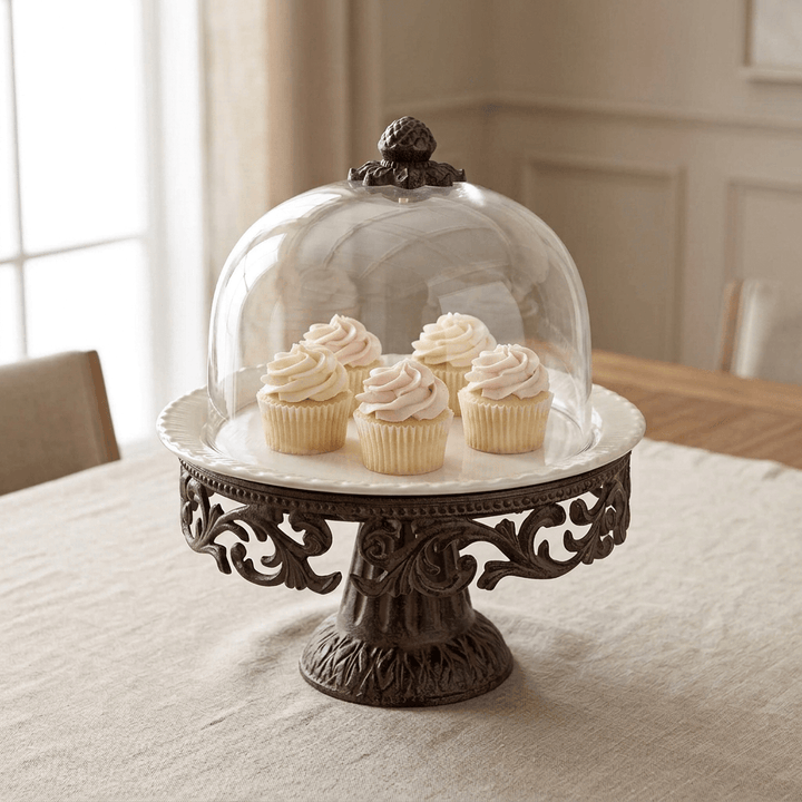 Bellavita ceramic cake pedestal displaying five pink and ivory frosted cupcakes beneath its glass dome on a linen-covered dining table.