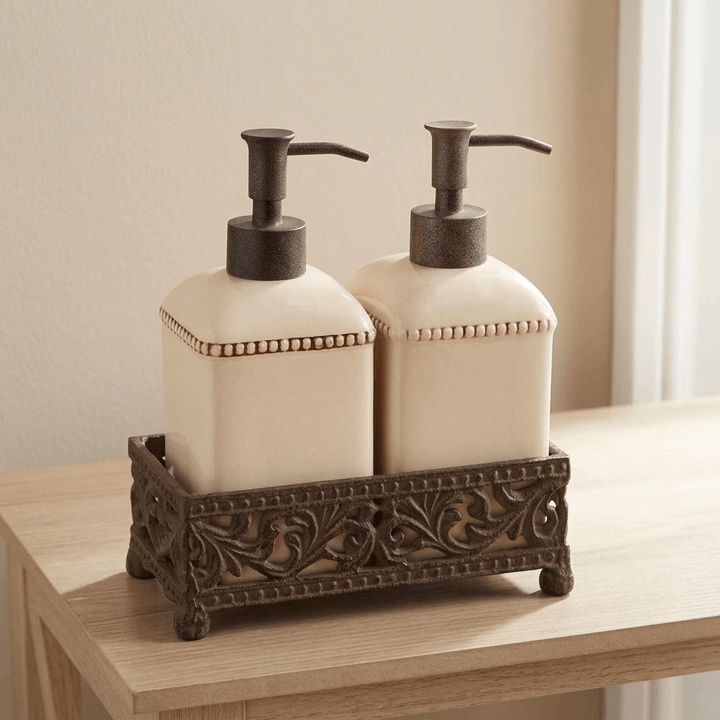 Two cream pump dispensers in their footed decorative metal base on a pale wooden console