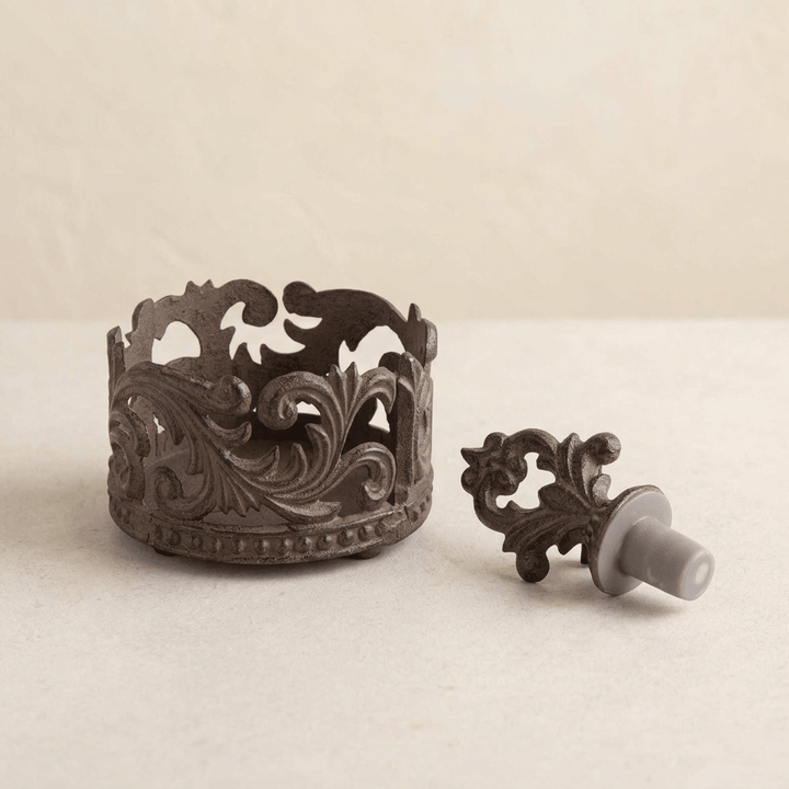 Ornate dark brown acanthus wine bottle holder and matching stopper displayed on a pale tabletop