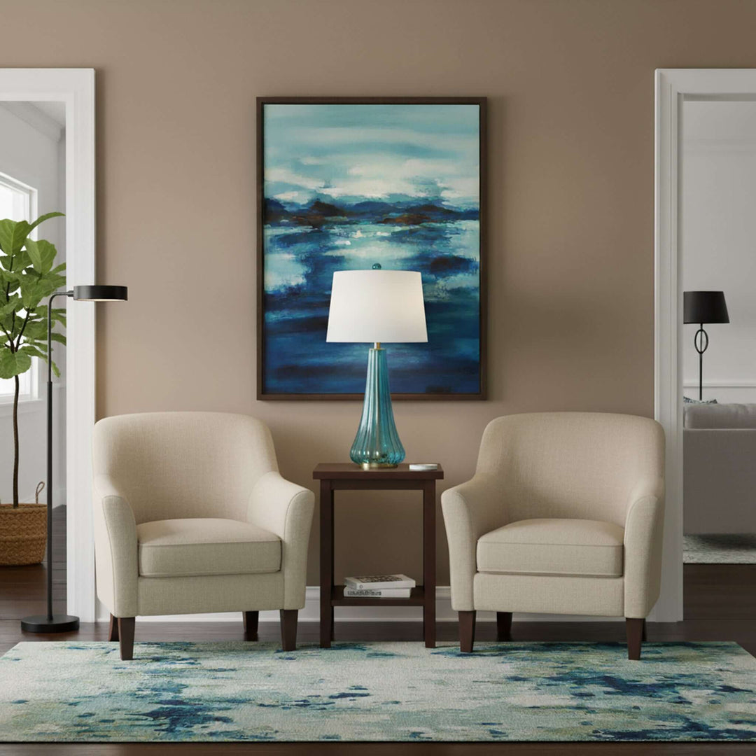 Living room with two beige armchairs, a side table with a lamp, and a colorful abstract painting on the wall.