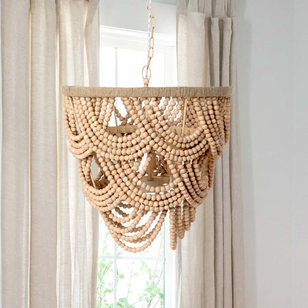 Wooden beaded chandelier hanging in front of sheer curtains
