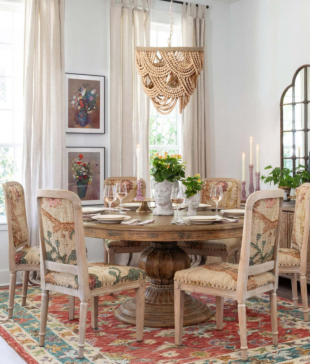 Dining room with wooden table and patterned chairs, decorated with candles and plants.
