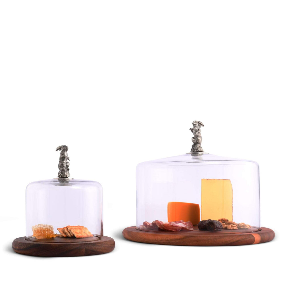 Two glass food display cloches with wooden bases on a white background