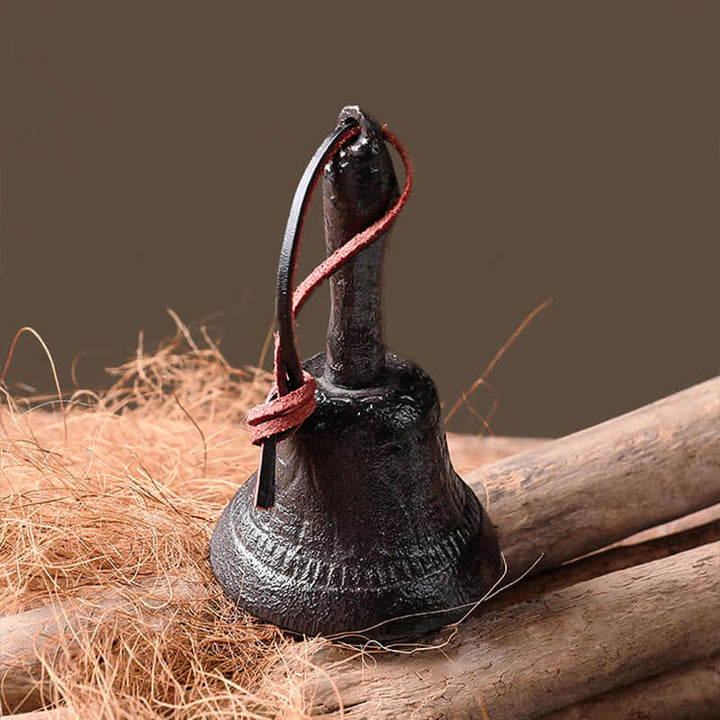 Black bell with a leatherstrap on a wooden surface with hay