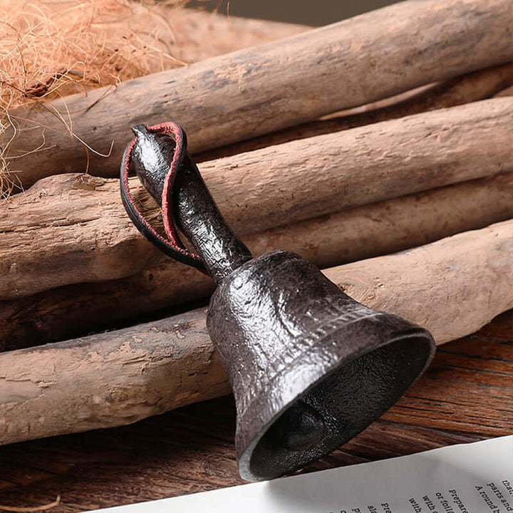 Black metal bell with leather strap on wooden logs