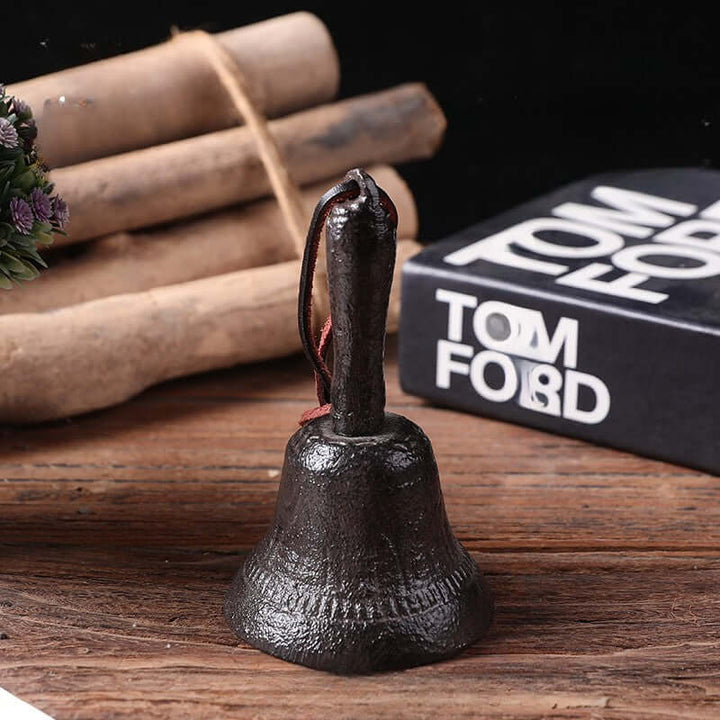 Black bell on a wooden surface with a blurred Tom Ford product in the background
